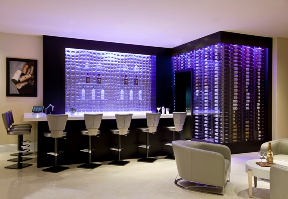 Adega da Wine Cellar Designs chamativa e luxuosa em sala de estar estilo bar com poltronas e cadeiras brancas